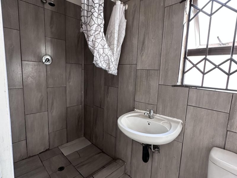 A functional bathroom featuring a walk-in shower, wall-mounted basin, and toilet, finished with grey wall and floor tiles.