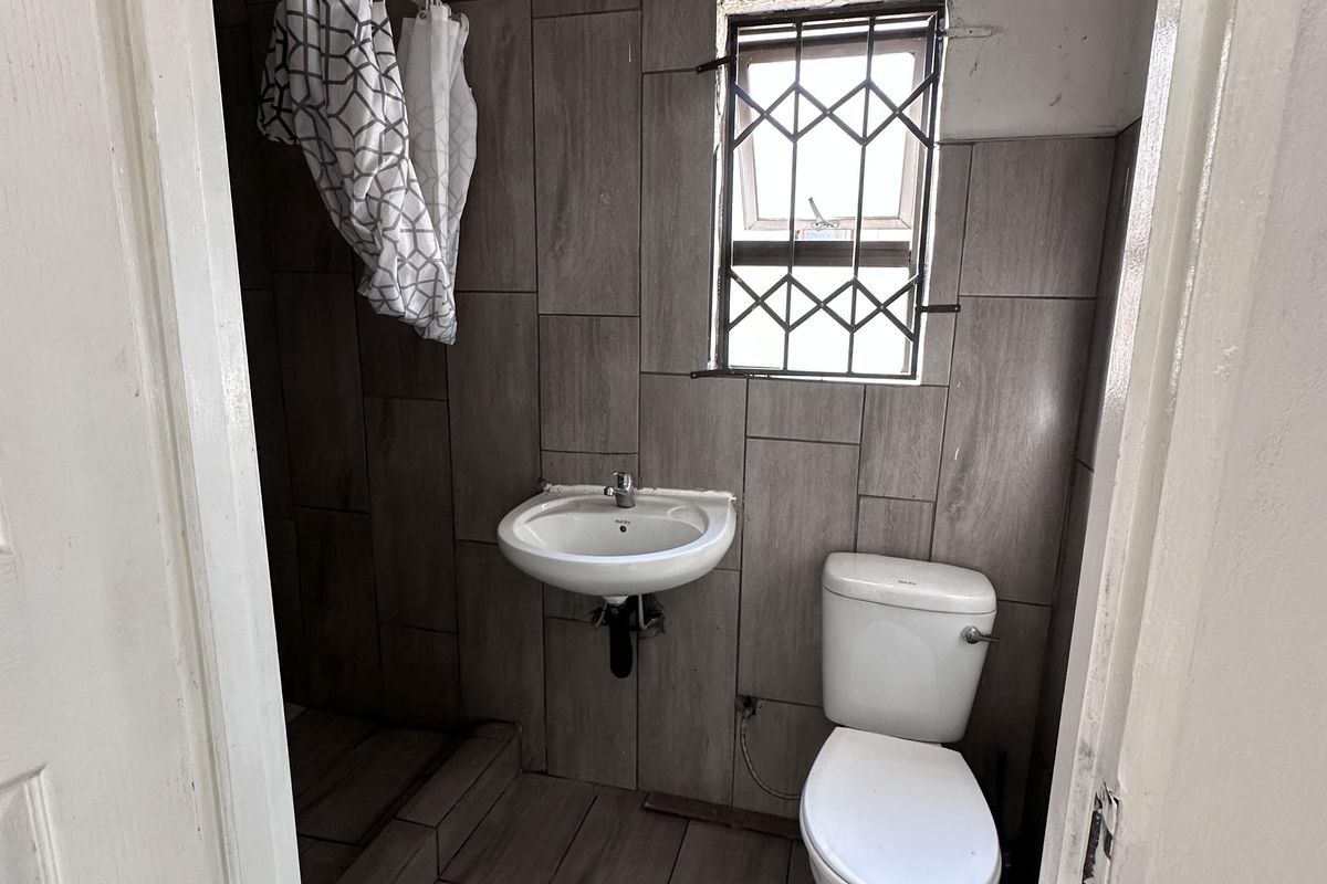 Compact bathroom featuring tiled walls and flooring, a wall-mounted basin, and a standard toilet, requiring minor cosmetic finishing to the walls and ceiling.