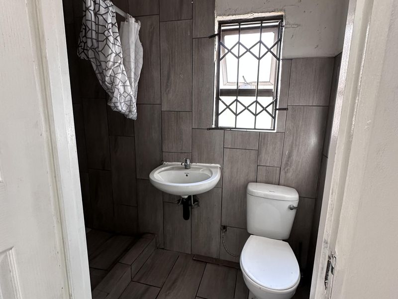 Compact bathroom featuring tiled walls and flooring, a wall-mounted basin, and a standard toilet, requiring minor cosmetic finishing to the walls and ceiling.