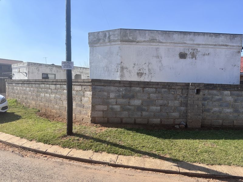 Exterior view of the property showing a concrete block boundary wall and a weathered plastered building facade.