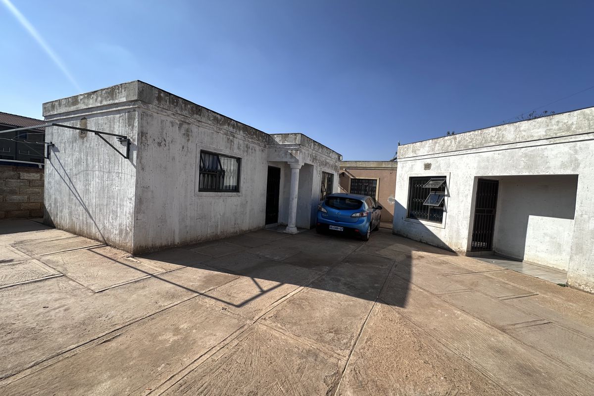 Exterior view of the apartment building featuring a concrete driveway, security bars on windows, and a covered entrance area.