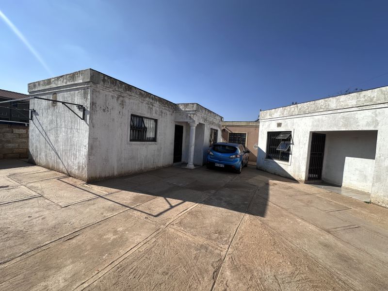 Exterior view of the apartment building featuring a concrete driveway, security bars on windows, and a covered entrance area.