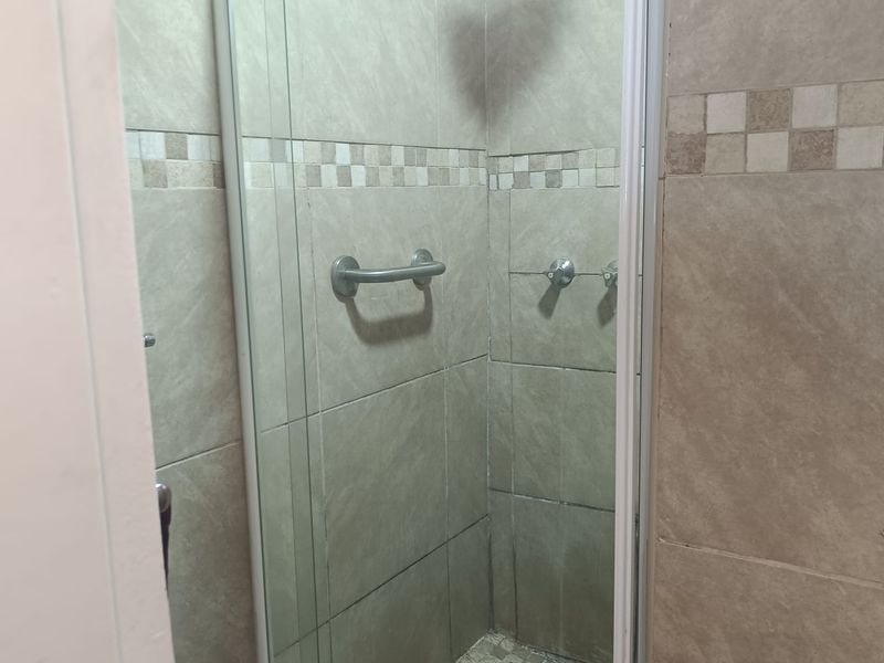 A functional shower stall featuring neutral wall and floor tiling, a glass enclosure, and a safety grab rail.