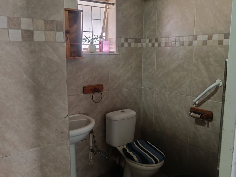 A functional bathroom featuring tiled walls and flooring, equipped with a pedestal basin, toilet, and safety grab rail.