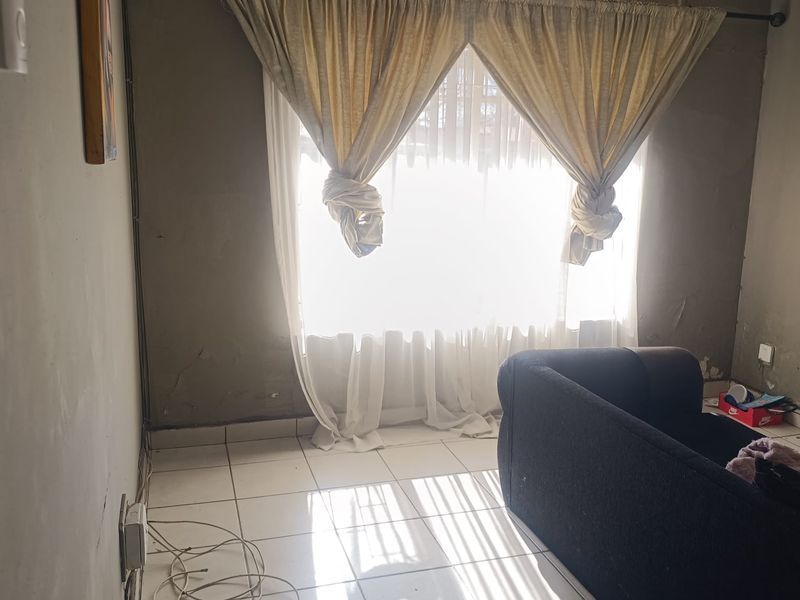 A living room space featuring tiled flooring and unfinished wall surfaces, requiring cosmetic attention to improve the overall aesthetic and finish.