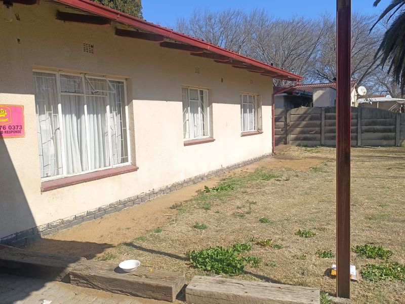 Rear view of the house featuring a covered patio area, steel window frames, and a large backyard with a concrete boundary wall.