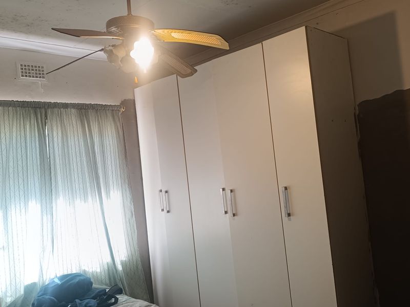 Bedroom featuring a built-in wardrobe and ceiling fan, requiring cosmetic attention to the ceiling and wall finishes.