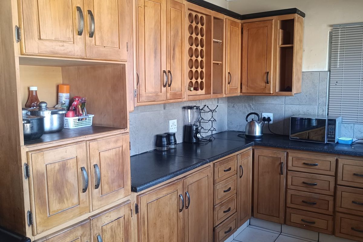 A functional kitchen featuring wooden cabinetry, dark laminate countertops, tiled backsplash, and tiled flooring, offering a classic layout with ample storage space.