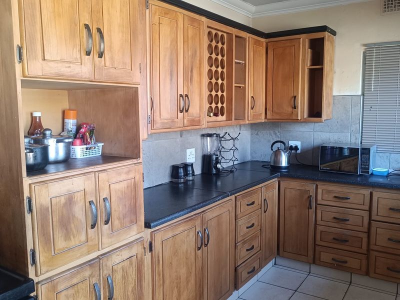 A functional kitchen featuring wooden cabinetry, dark laminate countertops, tiled backsplash, and tiled flooring, offering a classic layout with ample storage space.