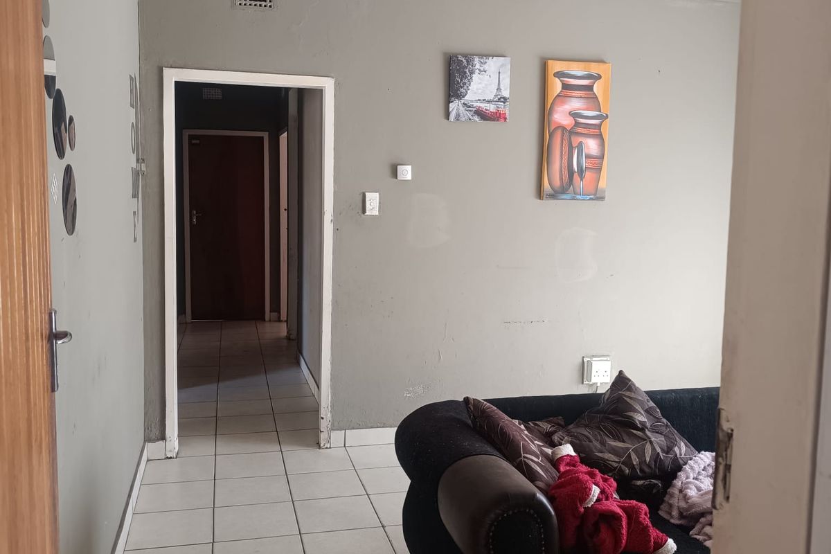 A living room area featuring ceramic floor tiles and neutral grey walls, providing a functional space with direct access to the hallway.