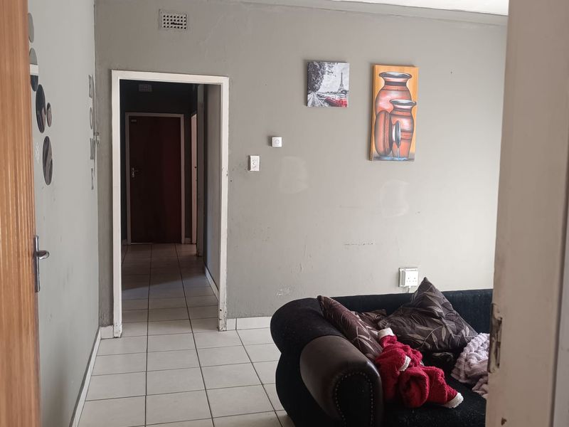 A living room area featuring ceramic floor tiles and neutral grey walls, providing a functional space with direct access to the hallway.