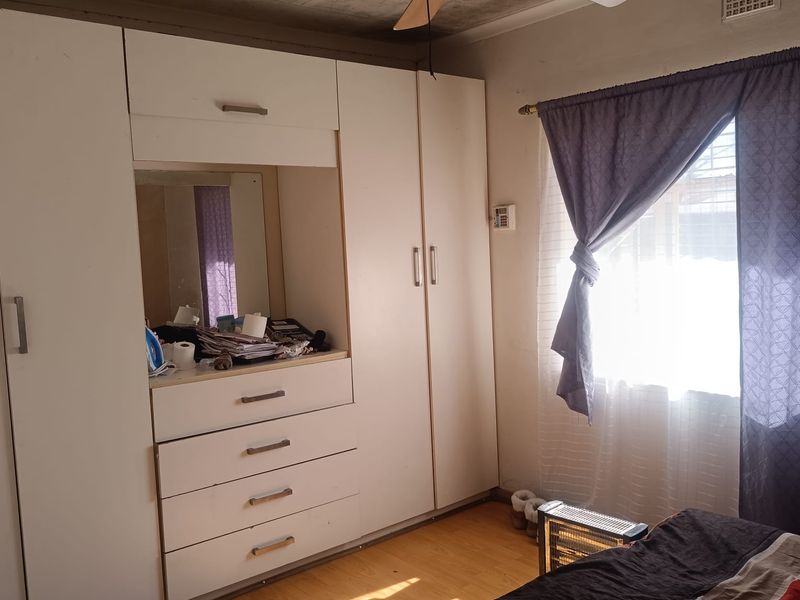 Bedroom featuring built-in cupboards, laminate flooring, and a ceiling fan. The ceiling shows visible signs of water damage and requires maintenance.
