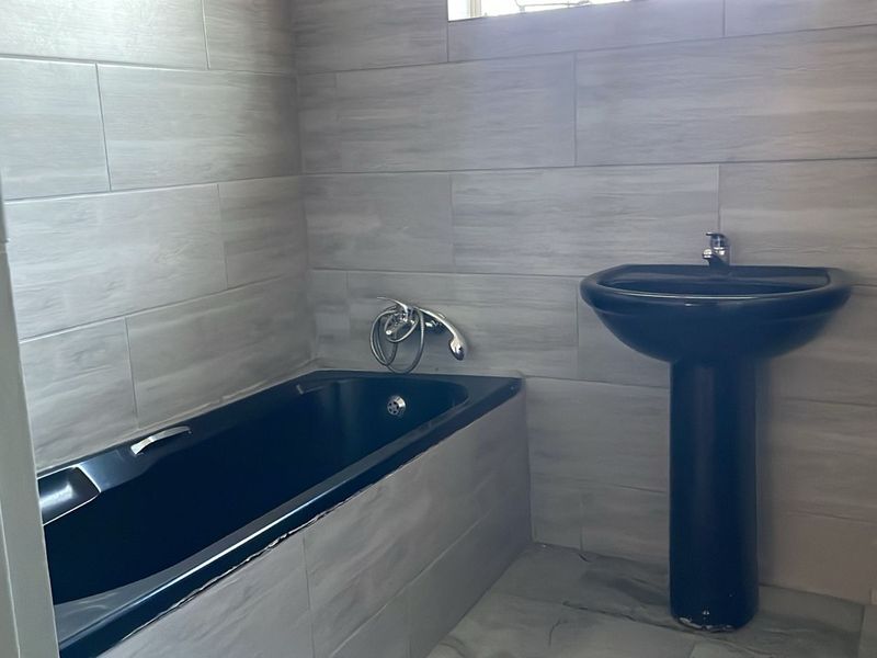 A modern bathroom featuring a black pedestal basin and matching built-in bathtub with neutral grey wall tiles.