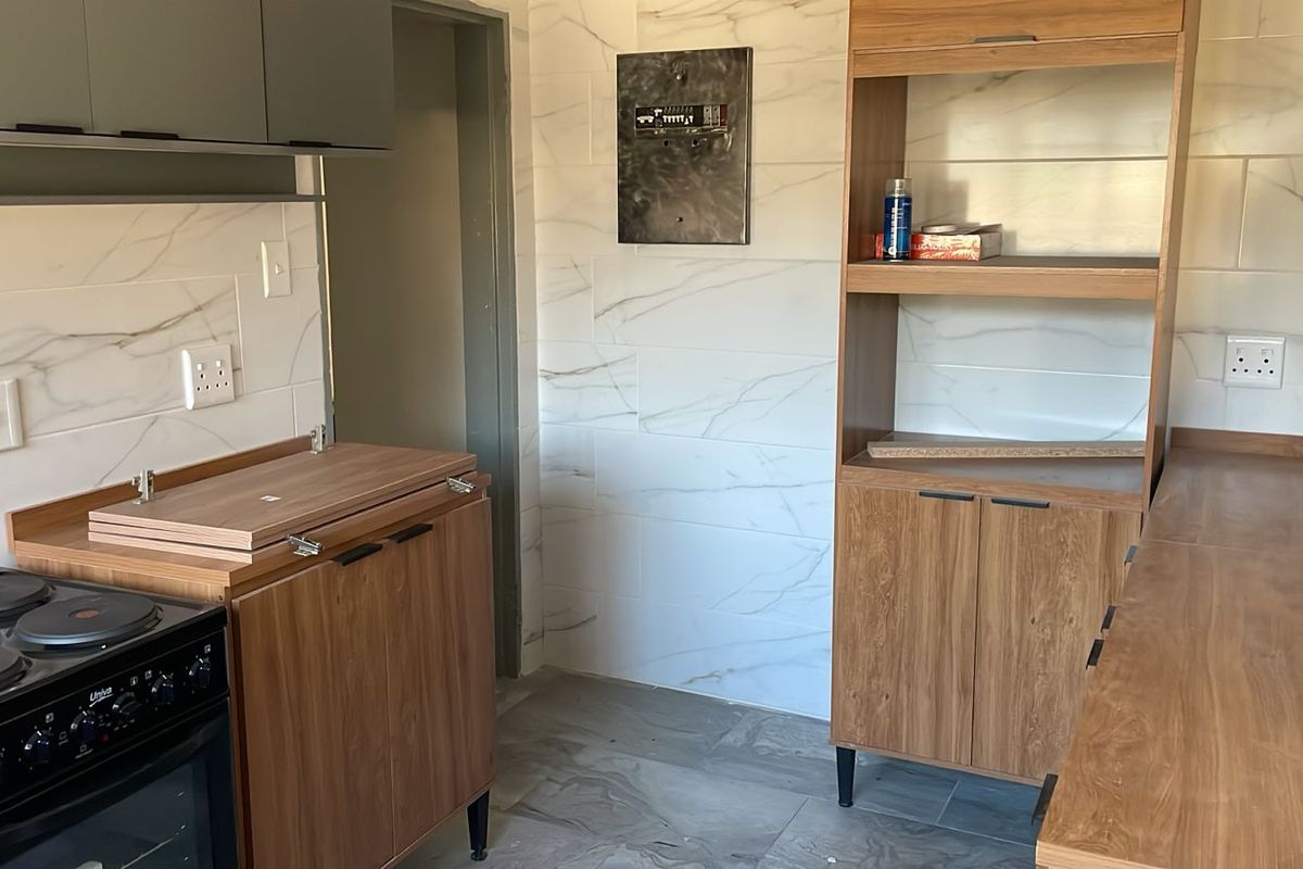 A compact kitchen featuring modern marble-look wall tiles, wood-finish cabinetry, and an electric stove, currently in a partially finished state.