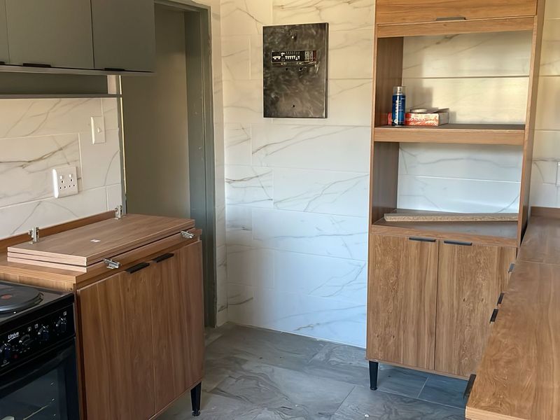 A compact kitchen featuring modern marble-look wall tiles, wood-finish cabinetry, and an electric stove, currently in a partially finished state.