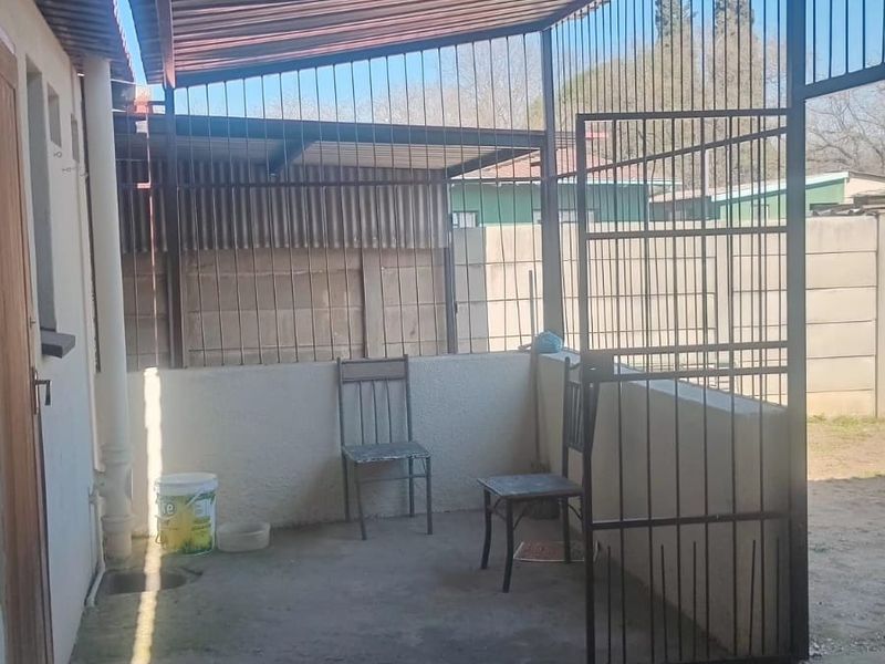 A covered outdoor patio area featuring a corrugated metal roof, security gate, and concrete flooring, providing a functional space for outdoor use.