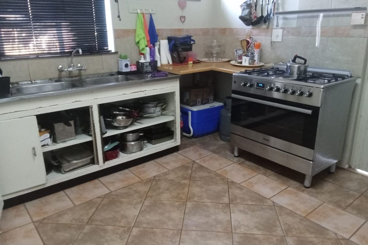 A functional kitchen featuring a stainless steel double sink, gas stove with oven, tiled backsplash, and ceramic floor tiles.