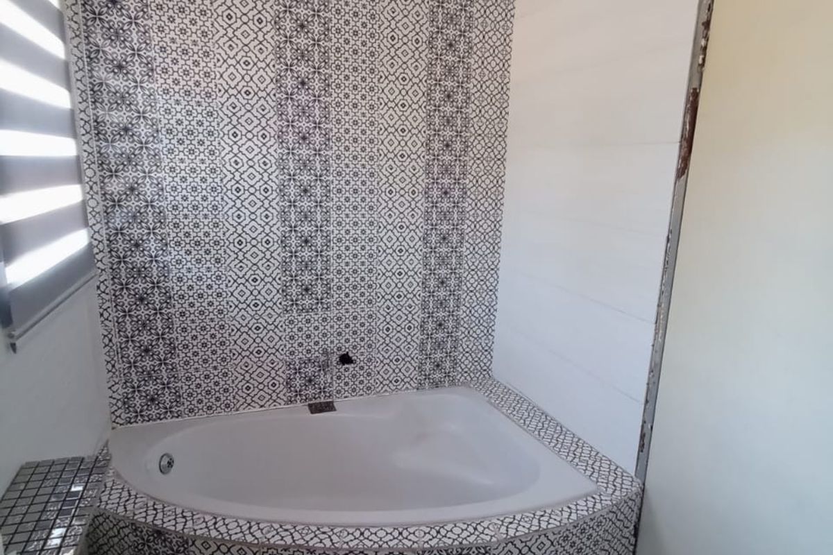 A bathroom featuring a corner bathtub with decorative patterned tiling on the walls and floor, complemented by a modern roller blind.
