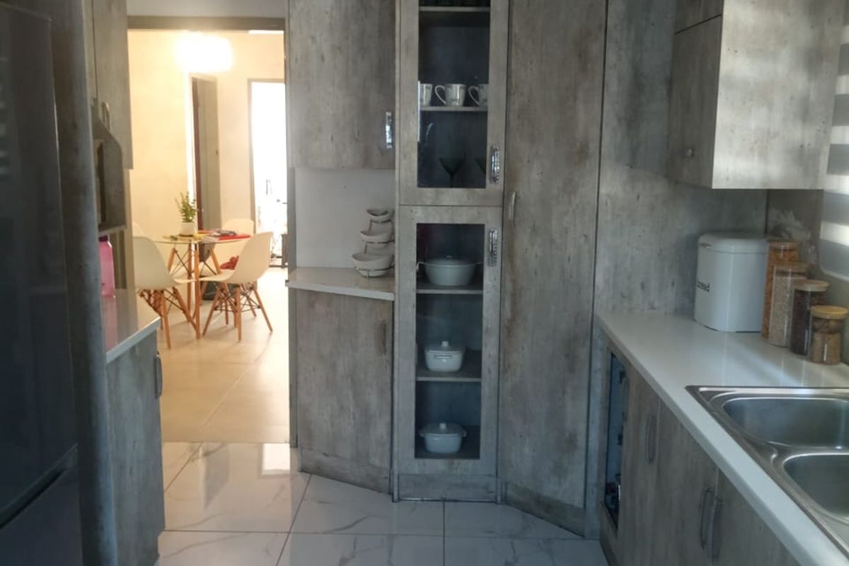 A modern kitchen featuring wood-grain cabinetry, marble-look floor tiles, and a stainless steel double sink, with an open view into the adjacent dining area.