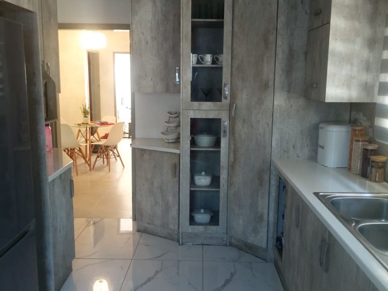 A modern kitchen featuring wood-grain cabinetry, marble-look floor tiles, and a stainless steel double sink, with an open view into the adjacent dining area.