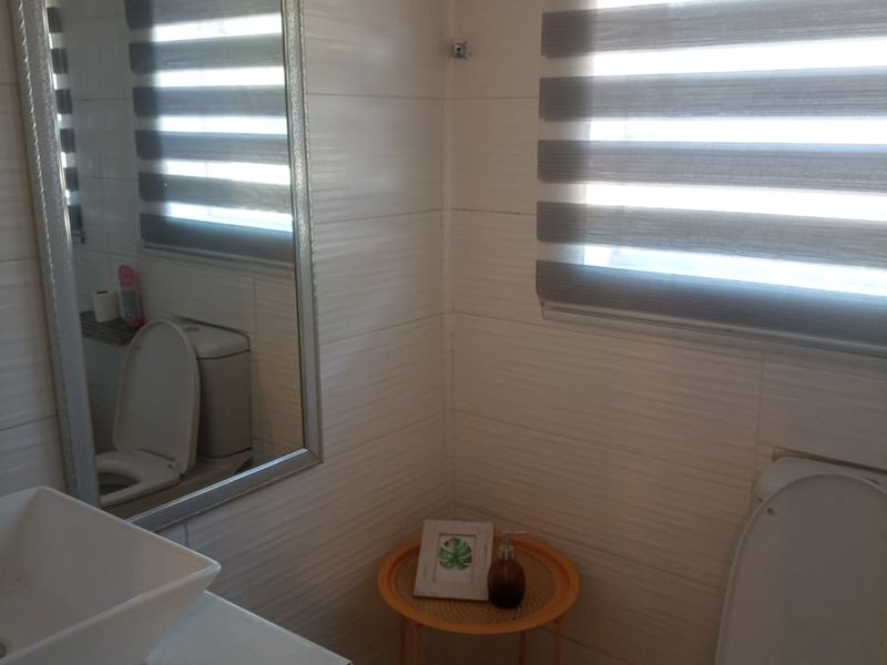 A compact bathroom featuring a modern vessel sink on a vanity, a toilet, tiled wall finishes, and roller blinds for privacy.