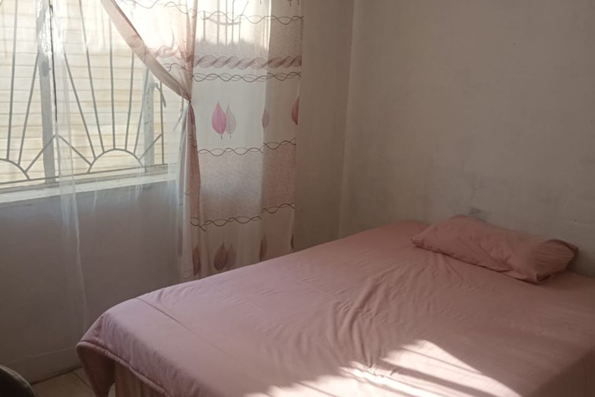A simple bedroom featuring tiled flooring and a window with security bars, requiring cosmetic updates to the wall finishes.
