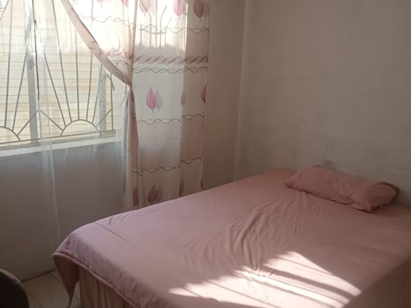 A simple bedroom featuring tiled flooring and a window with security bars, requiring cosmetic updates to the wall finishes.