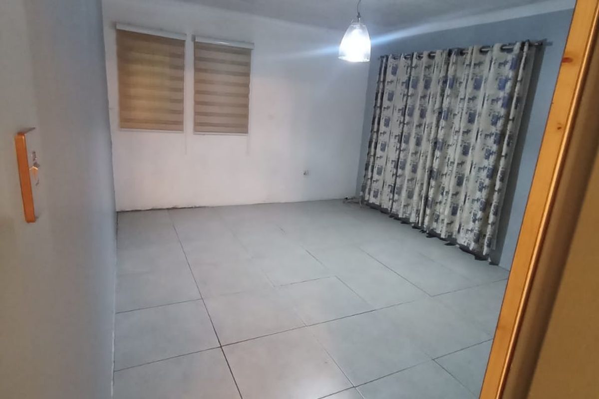An empty living room featuring large format floor tiles, a PVC ceiling, and roller blinds, providing a neutral canvas for interior design.