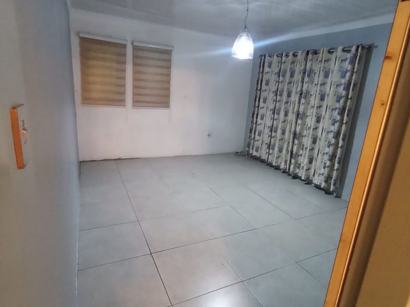 An empty living room featuring large format floor tiles, a PVC ceiling, and roller blinds, providing a neutral canvas for interior design.