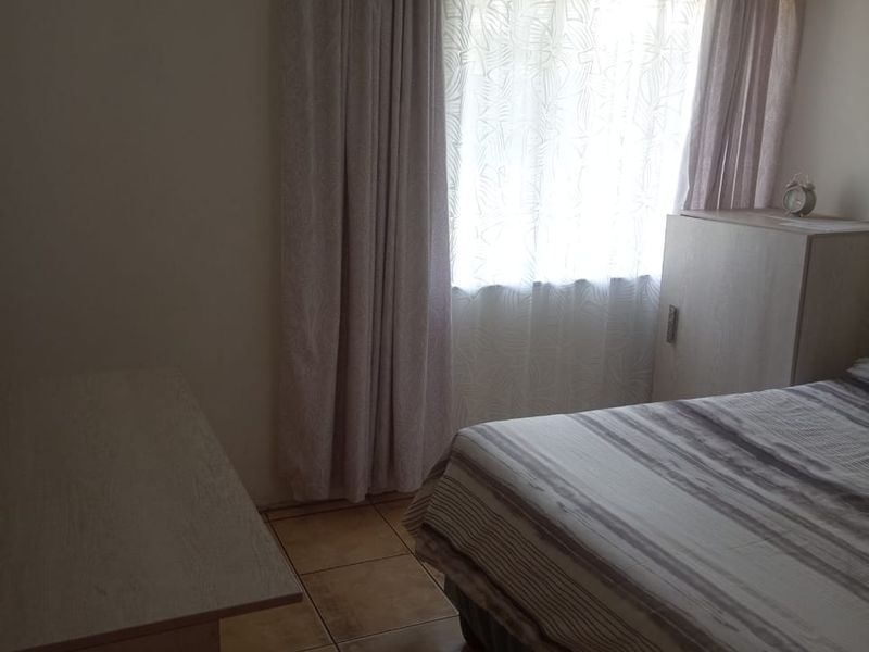 A functional bedroom featuring tiled flooring and natural light through a window with curtain tracks.