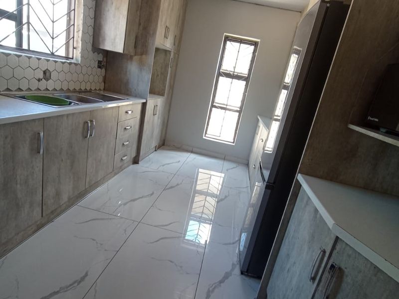 Modern kitchen featuring marble-effect floor tiles, hexagonal wall tiling, and ample built-in cabinetry with a clean, contemporary finish.