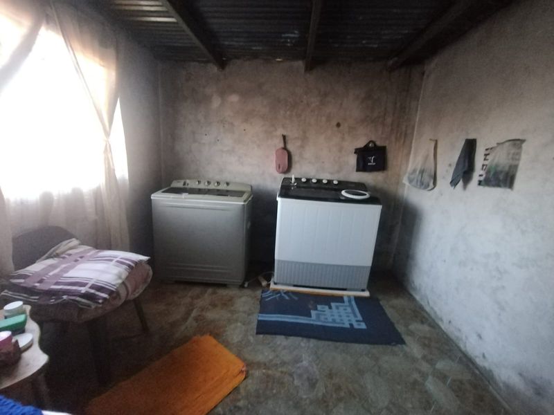 A functional laundry area featuring tiled flooring and exposed ceiling beams, requiring cosmetic updates to wall finishes and general maintenance.