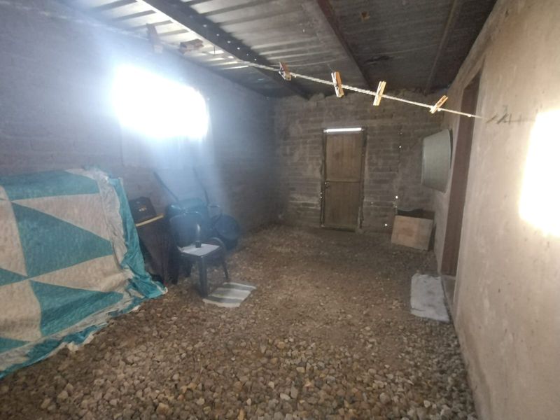 An unfinished utility space featuring exposed brick walls, a corrugated metal roof, and gravel flooring, suitable for storage or workshop conversion.