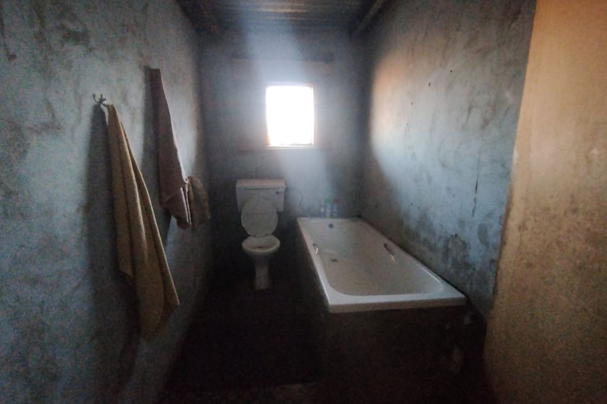 A basic bathroom featuring a bathtub and toilet with unfinished, weathered wall surfaces and a corrugated metal ceiling.