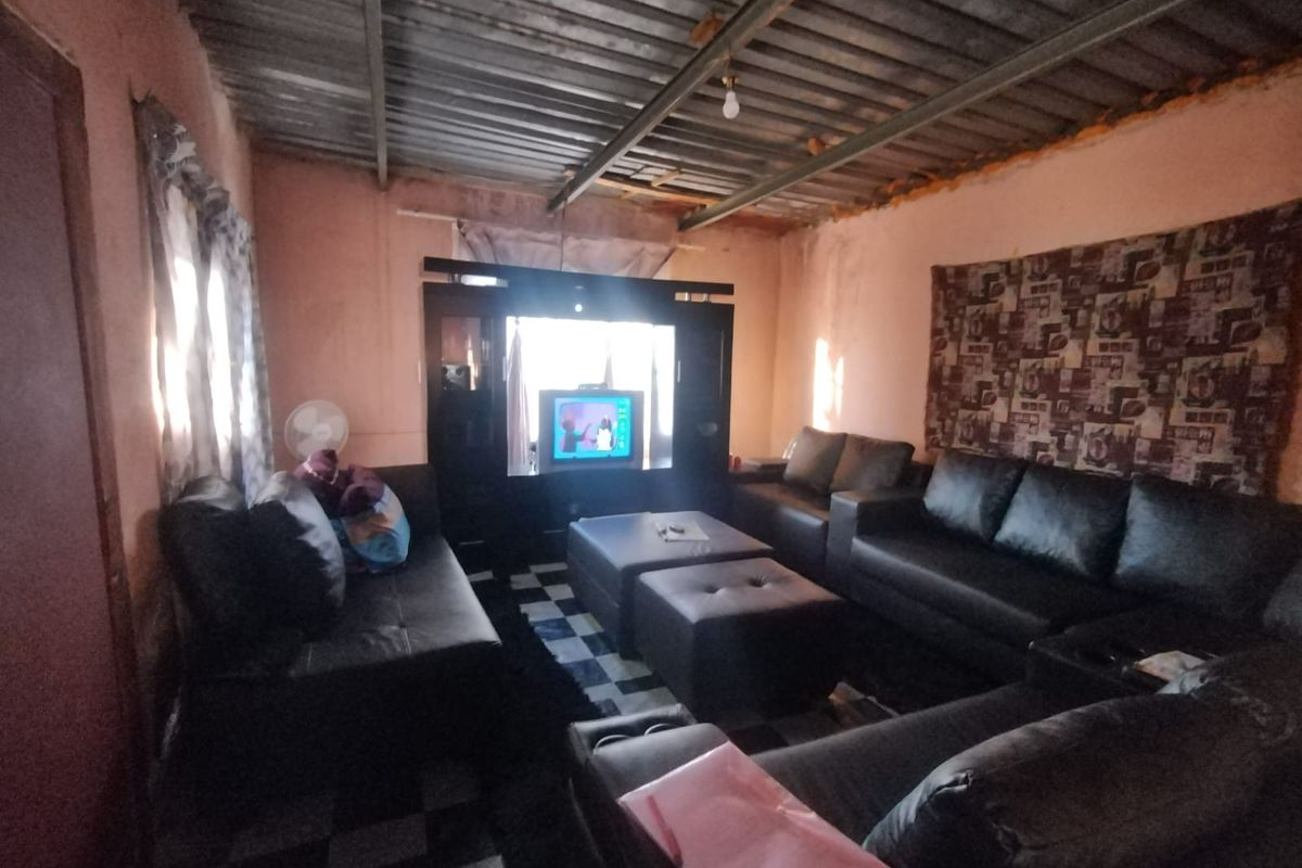 A living room featuring tiled flooring and an exposed corrugated metal ceiling, requiring cosmetic updates to improve the overall finish and aesthetic appeal.