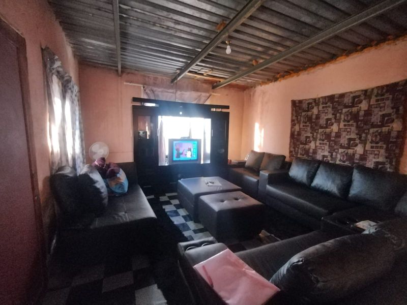 A living room featuring tiled flooring and an exposed corrugated metal ceiling, requiring cosmetic updates to improve the overall finish and aesthetic appeal.