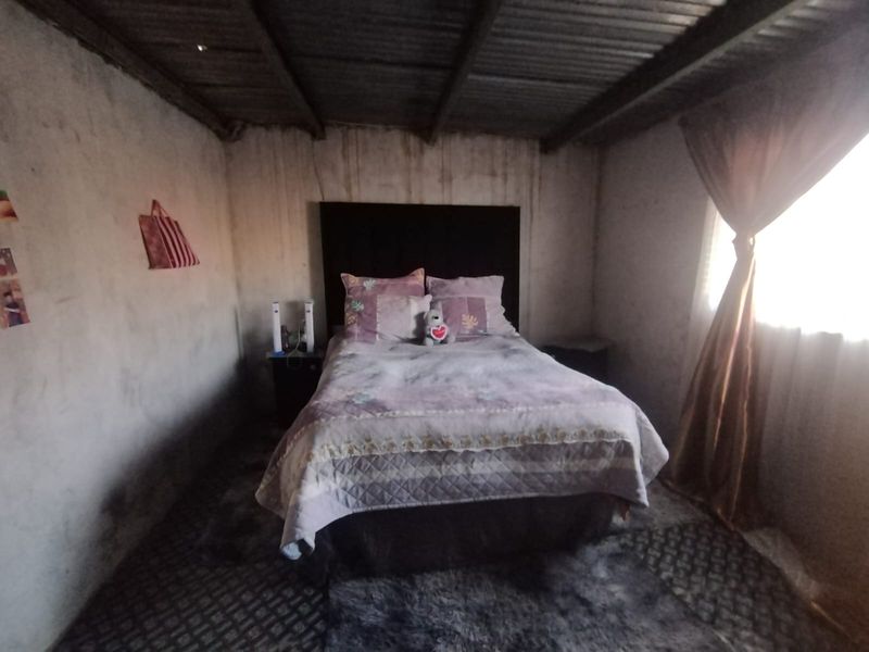 A bedroom featuring unfinished concrete walls and an exposed corrugated metal ceiling, requiring significant cosmetic updates and finishing to improve the living space.