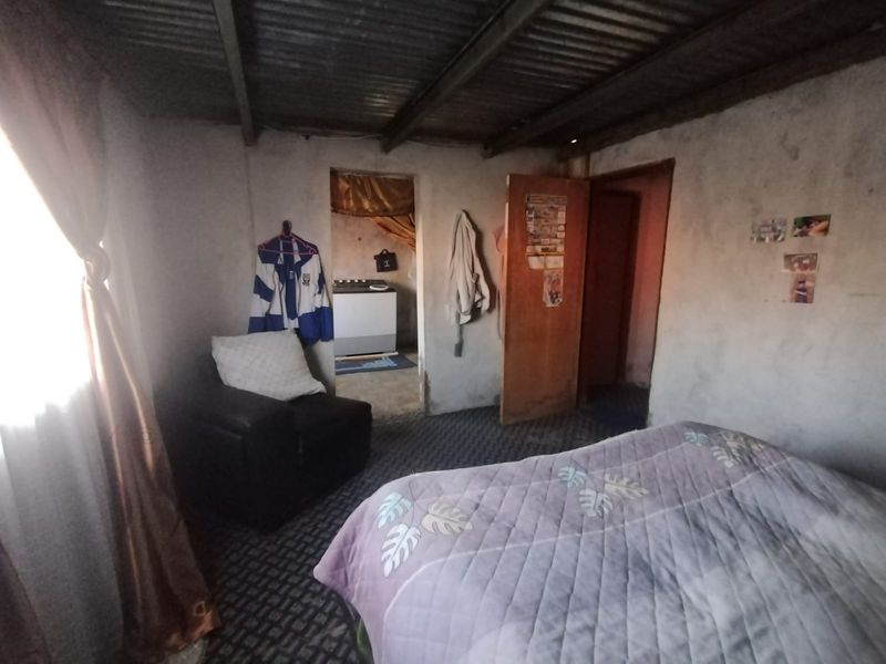 A bedroom featuring unplastered masonry walls and an exposed corrugated metal ceiling, offering a basic, rustic interior space.