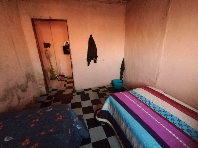 A bedroom featuring checkered floor tiles and plain wall surfaces, requiring cosmetic updates and repairs to improve the overall condition of the space.