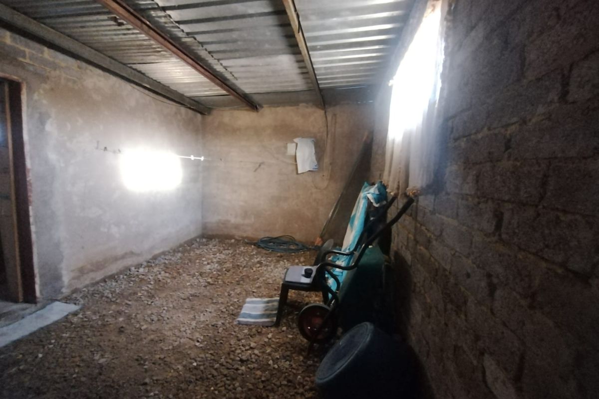 An unfinished utility space featuring exposed brick walls, a corrugated metal roof, and a gravel floor, suitable for storage or workshop conversion.