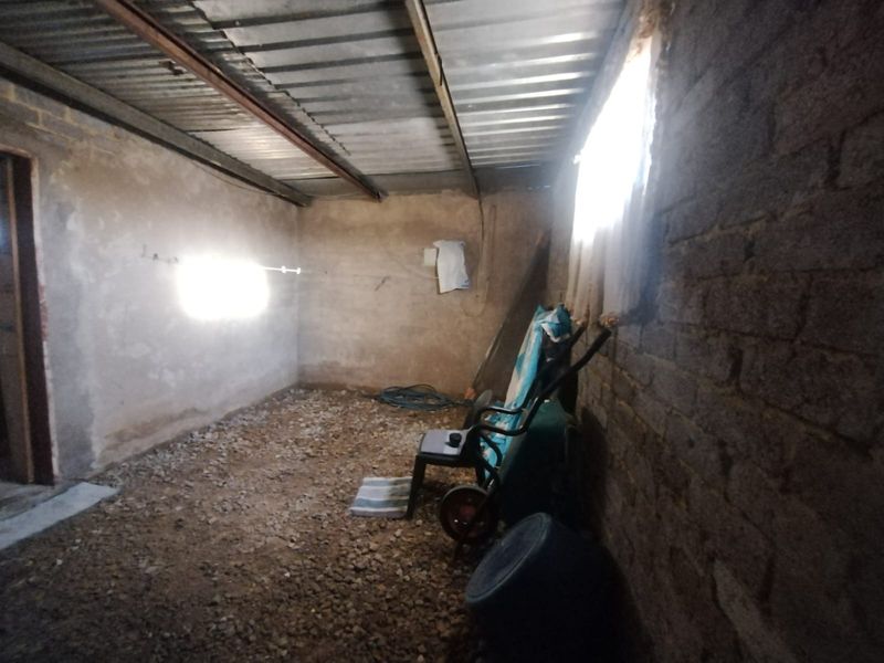 An unfinished utility space featuring exposed brick walls, a corrugated metal roof, and a gravel floor, suitable for storage or workshop conversion.
