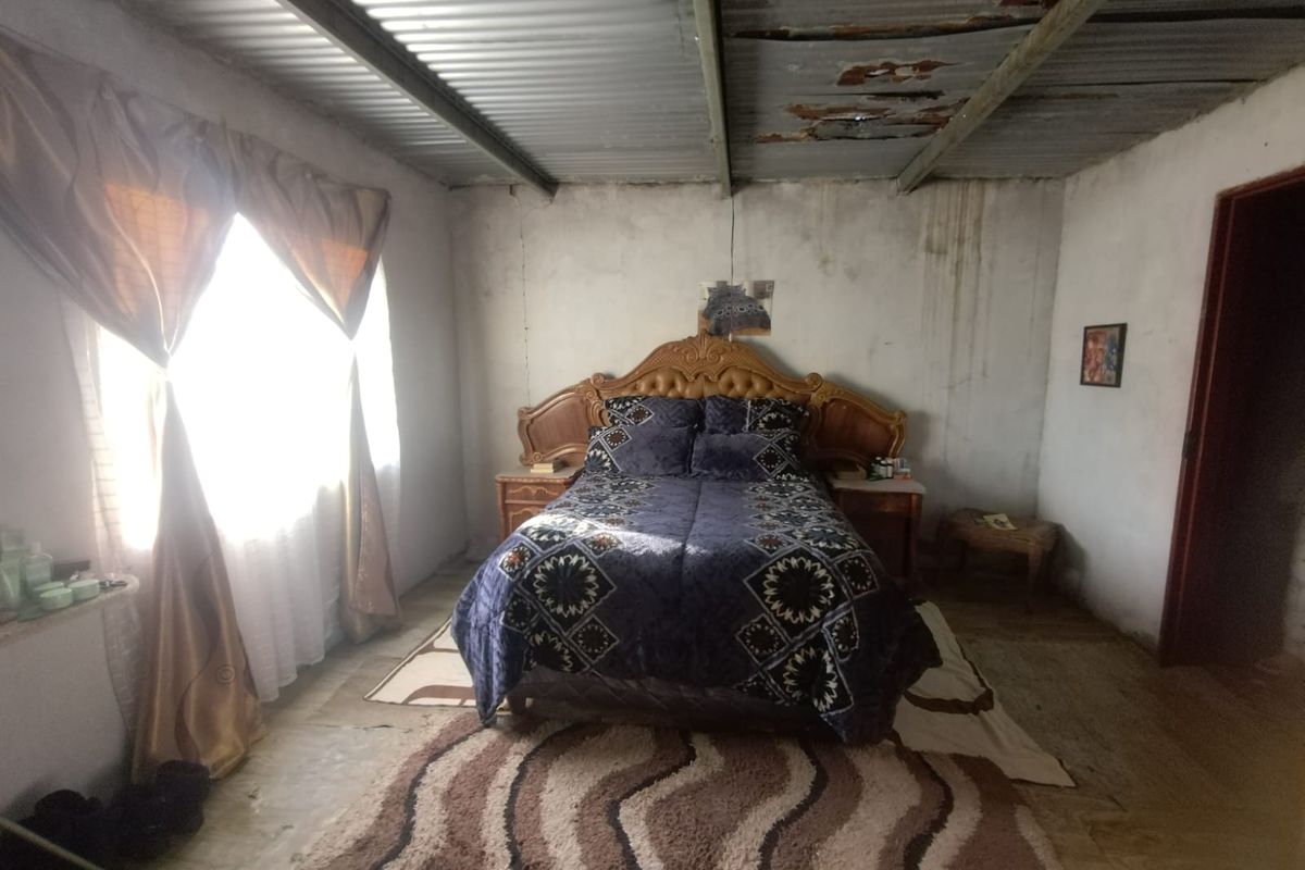A bedroom featuring a corrugated metal ceiling with visible signs of wear and unfinished wall surfaces, offering potential for renovation and modernization.