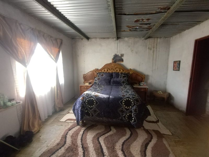 A bedroom featuring a corrugated metal ceiling with visible signs of wear and unfinished wall surfaces, offering potential for renovation and modernization.