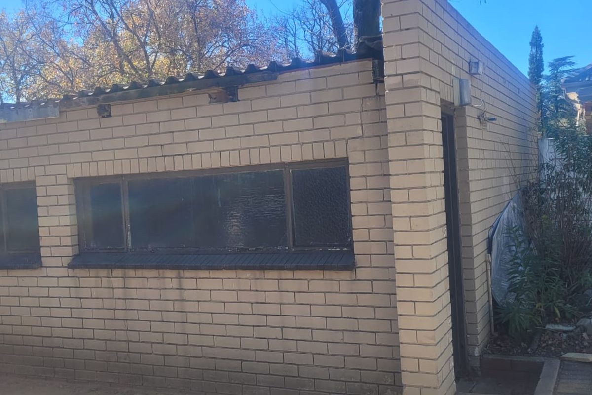 Rear view of a brick outbuilding featuring metal roof sheeting and fixed windows, showing signs of wear and maintenance requirements.