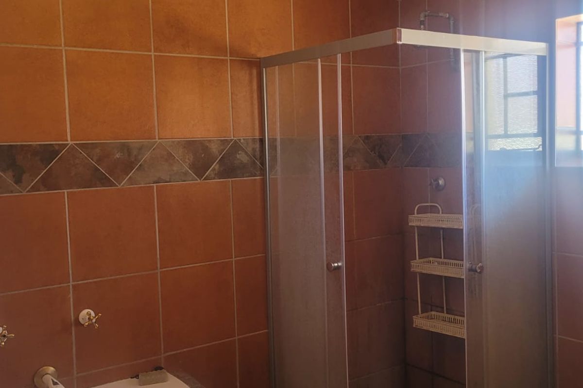 A functional bathroom featuring a shower enclosure, ceramic wall tiling, and a pedestal washbasin with natural light from a window.