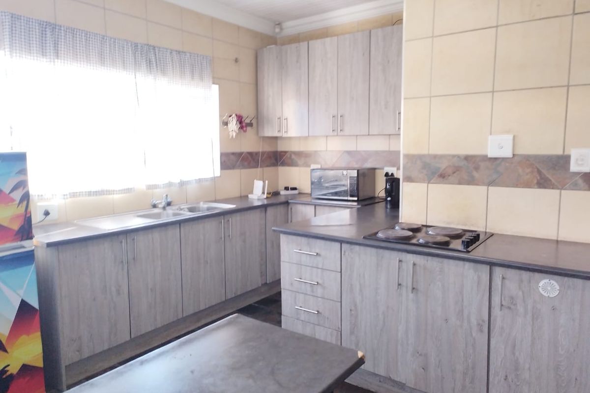 A functional kitchen featuring wood-look laminate cabinetry, tiled splashbacks, a double bowl sink, and a built-in hob with ample counter space.