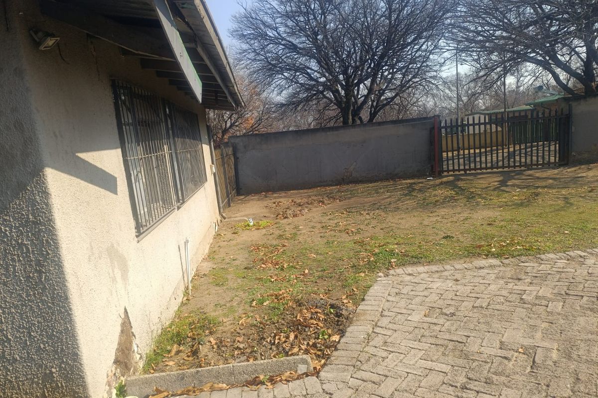 Rear exterior view of the property featuring a paved area, perimeter wall, metal gate, and security bars on the windows.