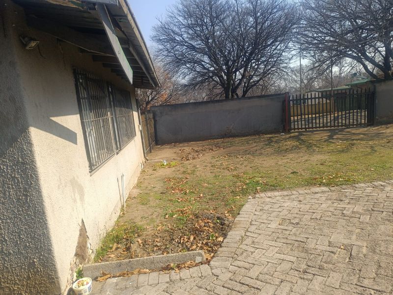 Rear exterior view of the property featuring a paved area, perimeter wall, metal gate, and security bars on the windows.