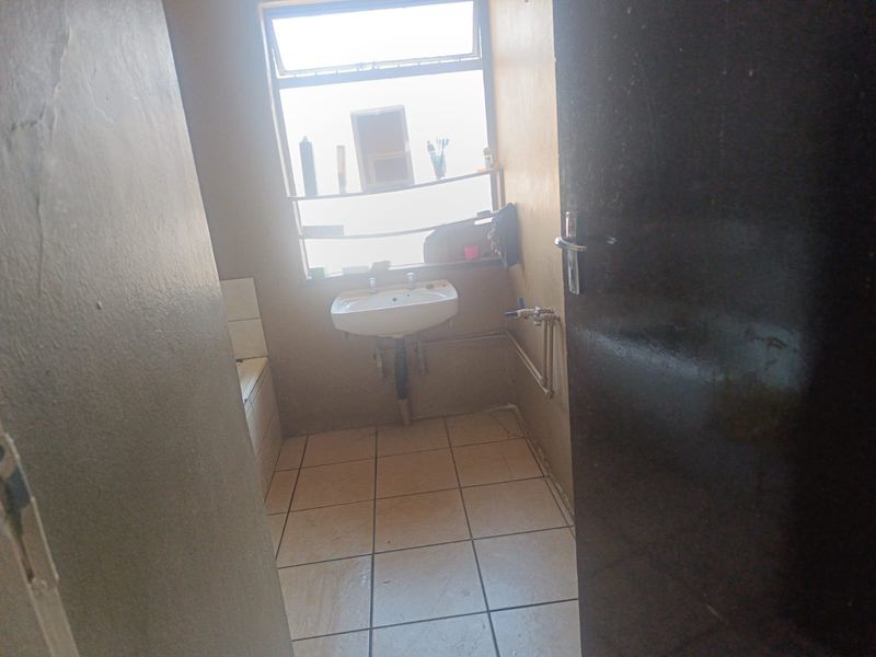 A basic bathroom featuring a pedestal washbasin, tiled flooring, and a window, currently in need of cosmetic updates and maintenance.