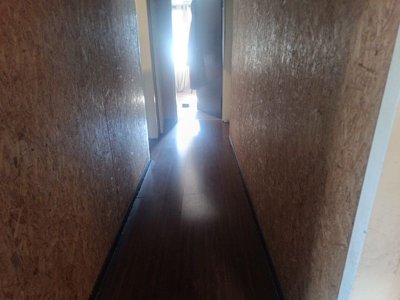 A narrow hallway featuring dark laminate flooring and unfinished OSB wall paneling, requiring cosmetic updates to improve the aesthetic appeal.